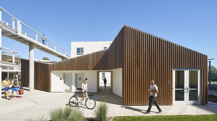 Image of the entrance to the San Joaquin Housing complex with wooden panelled facade beneath a bridge and pedestrian walkway.