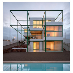 A photograph of a contemporary house with a pool in the front and a sunset in the background