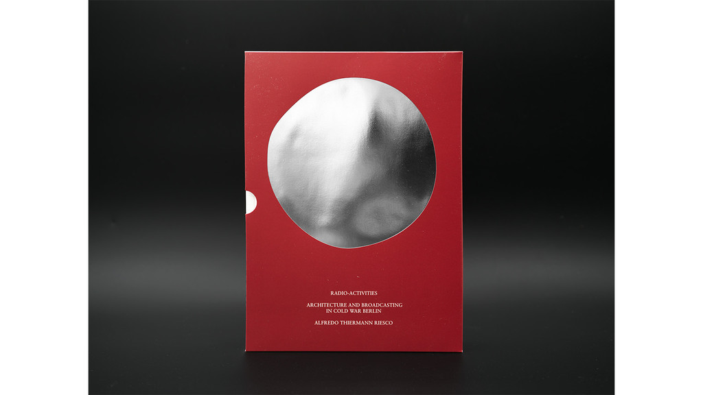 A black background with bit of shine across the middle, and a dark red book cover right in the center, with a silver circle on the cover