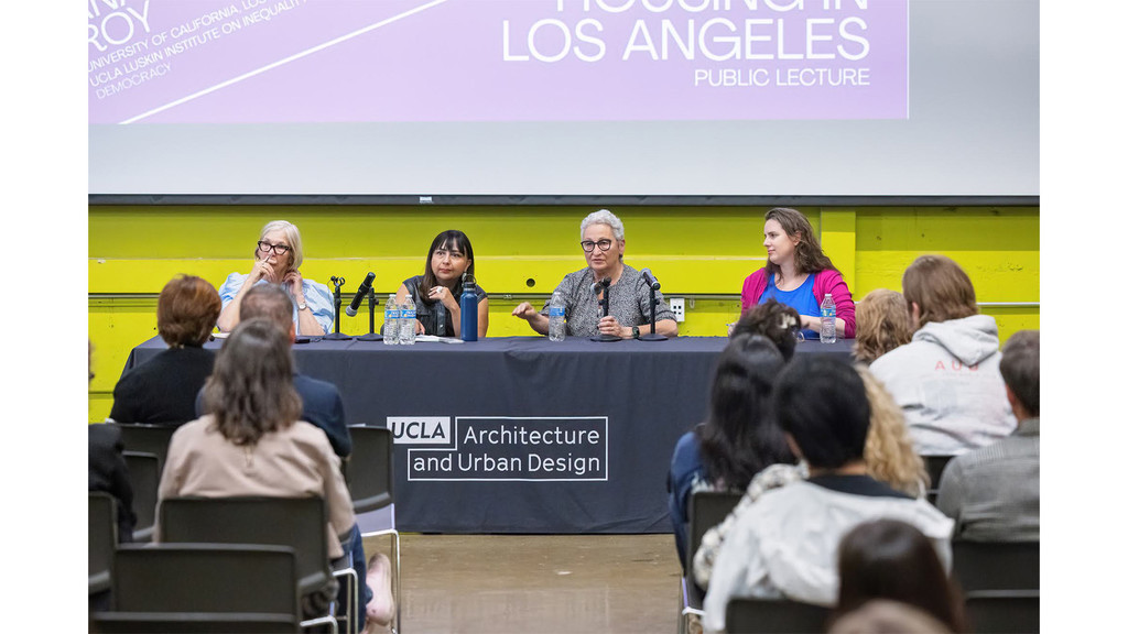 Four women seated at a table with a black tablecloth, facing the camera, in conversation with one another