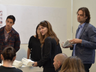 Four people are standing and discussing images on a wall, with a woman in the middle smiling and looking over to the audience