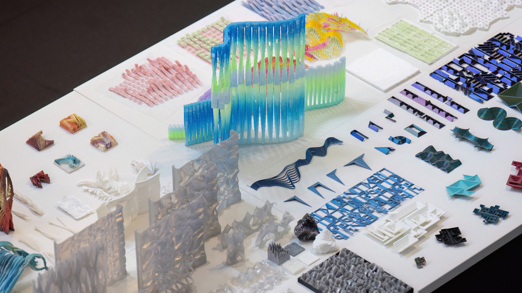 A photograph showing various 3D-printed models and samples of building facades, spread across a white table