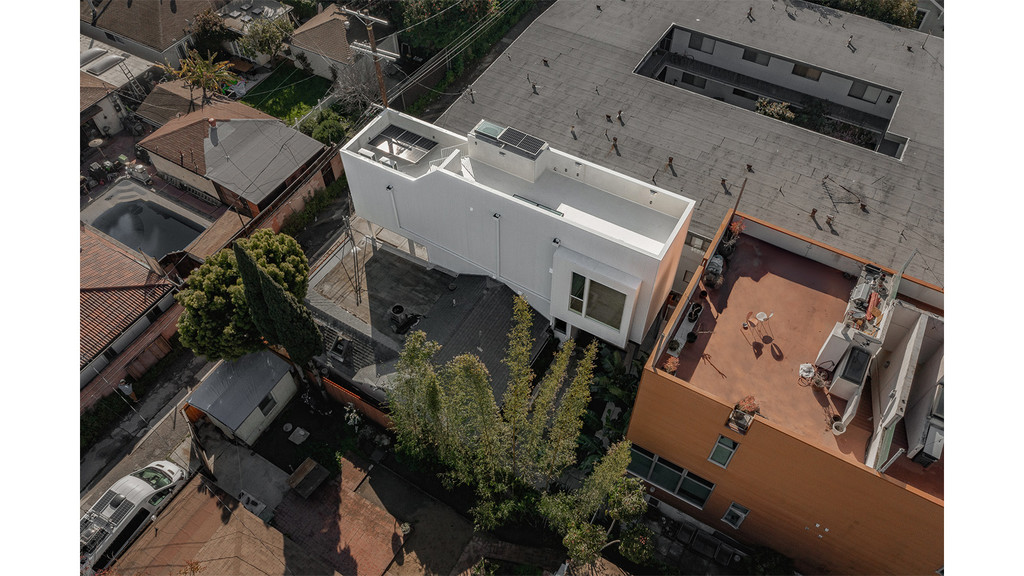 A photograph taken from the sky, showing a slender, two-story tall white building shaped like a rectangle, surrounded by rectangular homes in a residential neighborhood